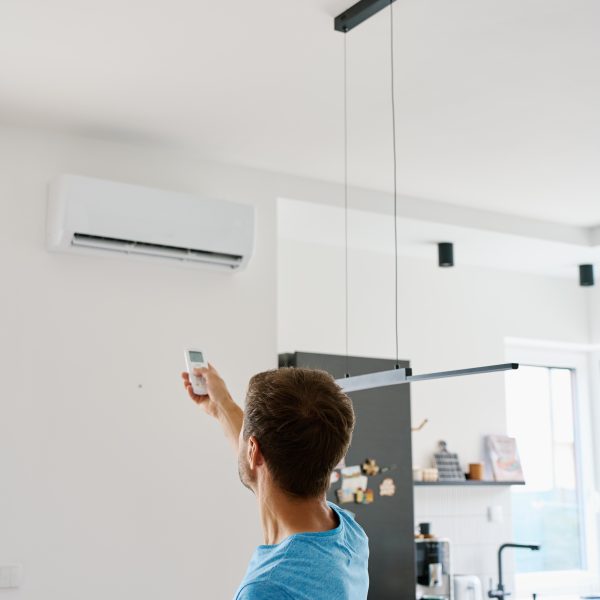 man operating air conditioner with remote control modern kitchen interior